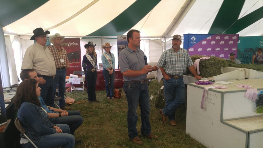 Brian Wing, President of the Wyoming Hay and Forage Association talks at the awards ceremony on Tuesday afternoon. Morgan Wallace (left), 2018 Miss Rodeo Wyoming, Abby Hayduck (right), Miss Rodeo Wyoming 2017, and ? (right of Brian), from Brown Company were all present to present awards. 